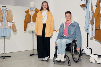 Isabel Niemann steht zwischen Kleiderpuppen mit ihrer Kollektion, daneben Kai Kramer im Rollstuhl sitzend